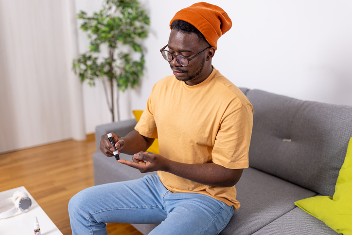 Young African American Man Prioritizes Health by Measuring Blood Sugar Level on the Sofa