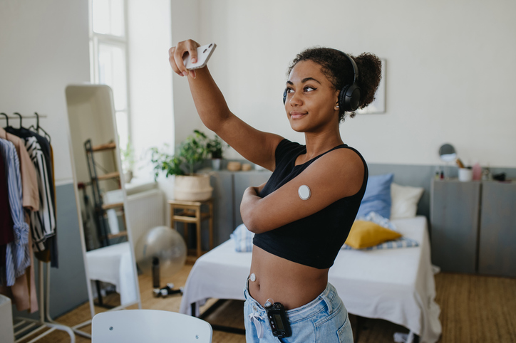 Beautiful diabetic girl taking a selfie, having an insulin pump and a continuous glucose monitor on her arm. Teenage girl is not ashamed of having diabetes, sharing her life with a chronic illness on social media.