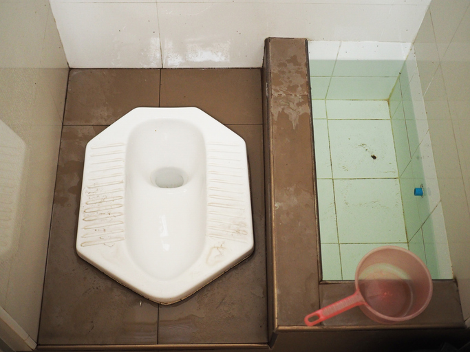 Top view Thai wet ceramic squat pot toilet with water basin and bucket, brown floor
